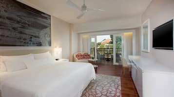 A hotel room with a large bed, a desk, a chair, a TV, and a balcony with a view of the city.