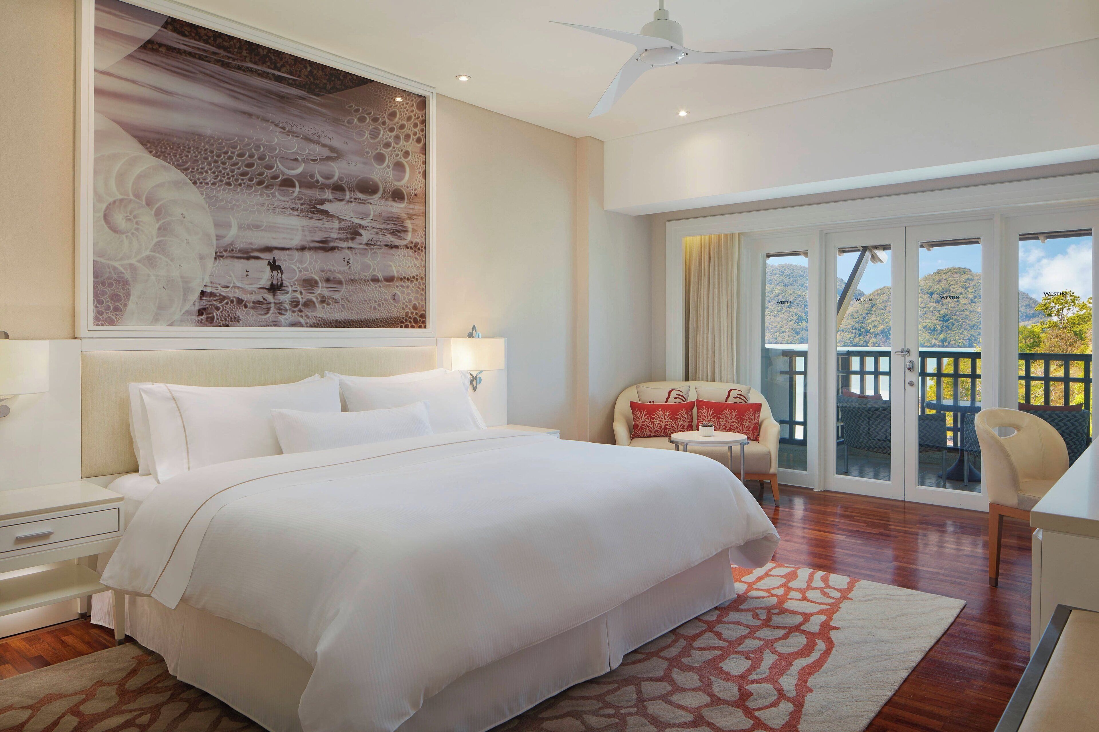 A spacious bedroom with a large bed, a ceiling fan, and a view of the outdoors through a sliding glass door.