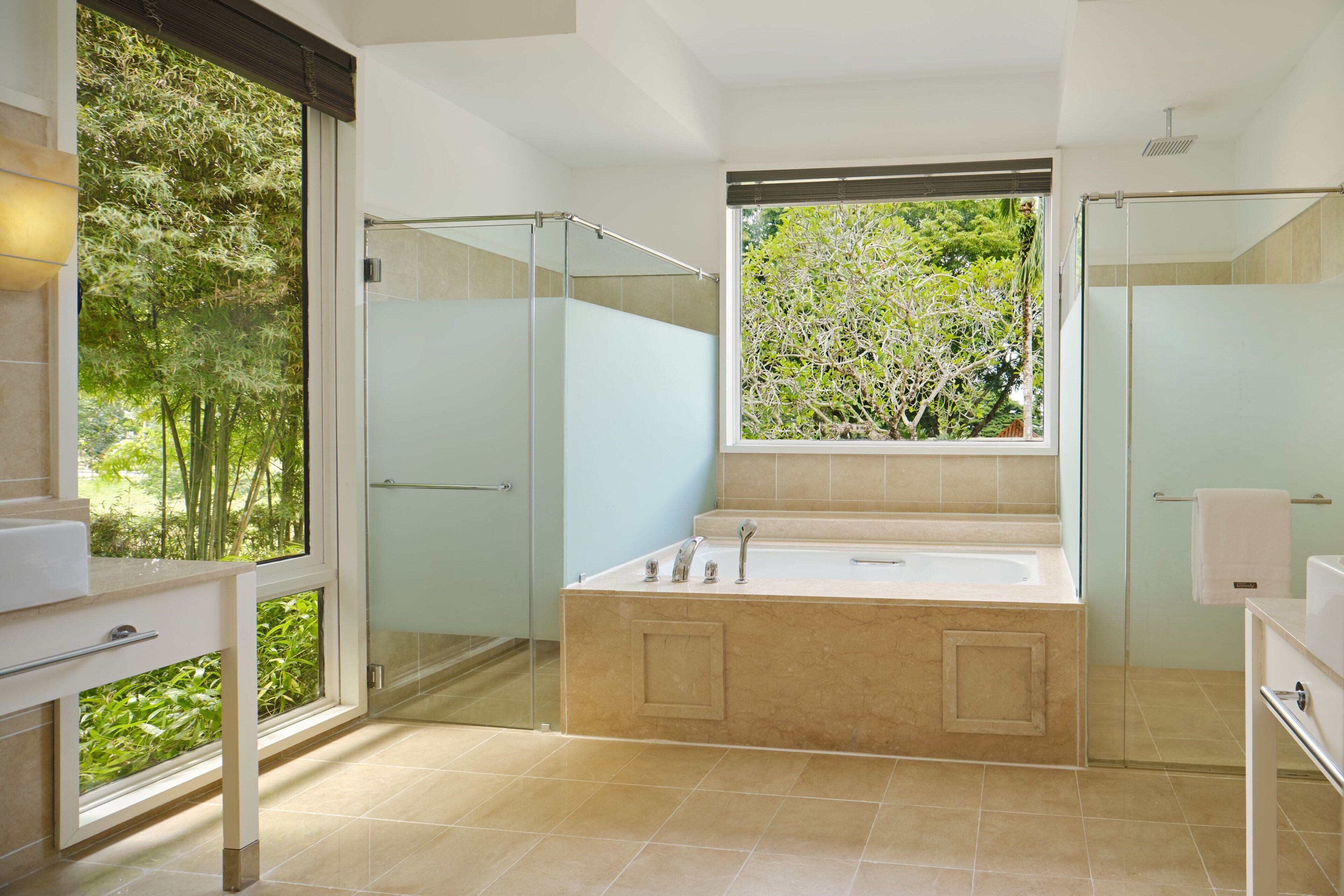A modern bathroom with a glass-enclosed shower, a large bathtub, and a view of greenery through a window.