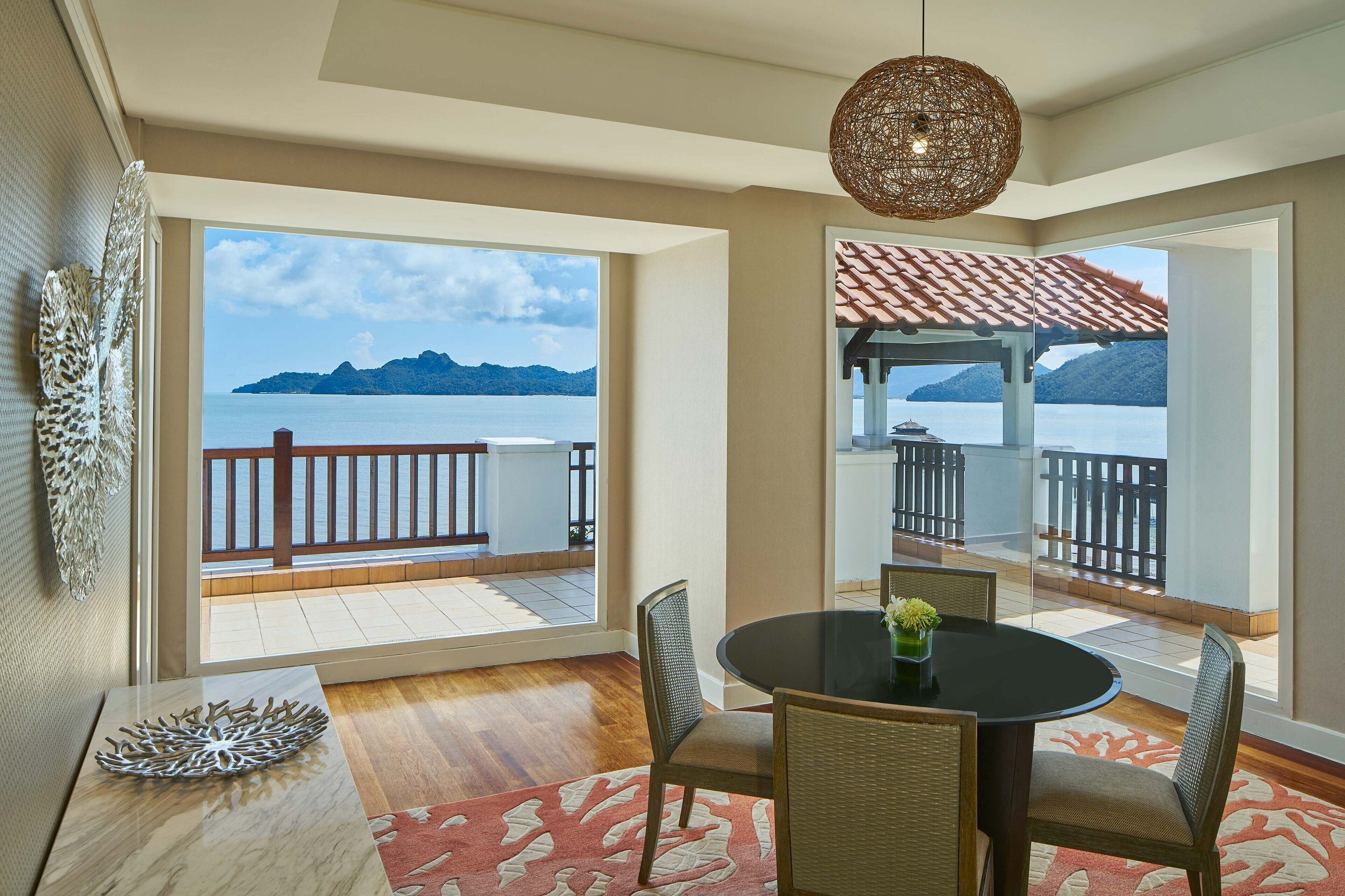 Un coin repas avec vue sur la mer, une table ronde, des chaises en osier et un luminaire suspendu.