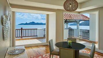 Un coin repas avec vue sur la mer, une table ronde, des chaises en osier et un luminaire suspendu.