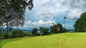 A golf course with a flagstick, surrounded by trees and a cloudy sky.