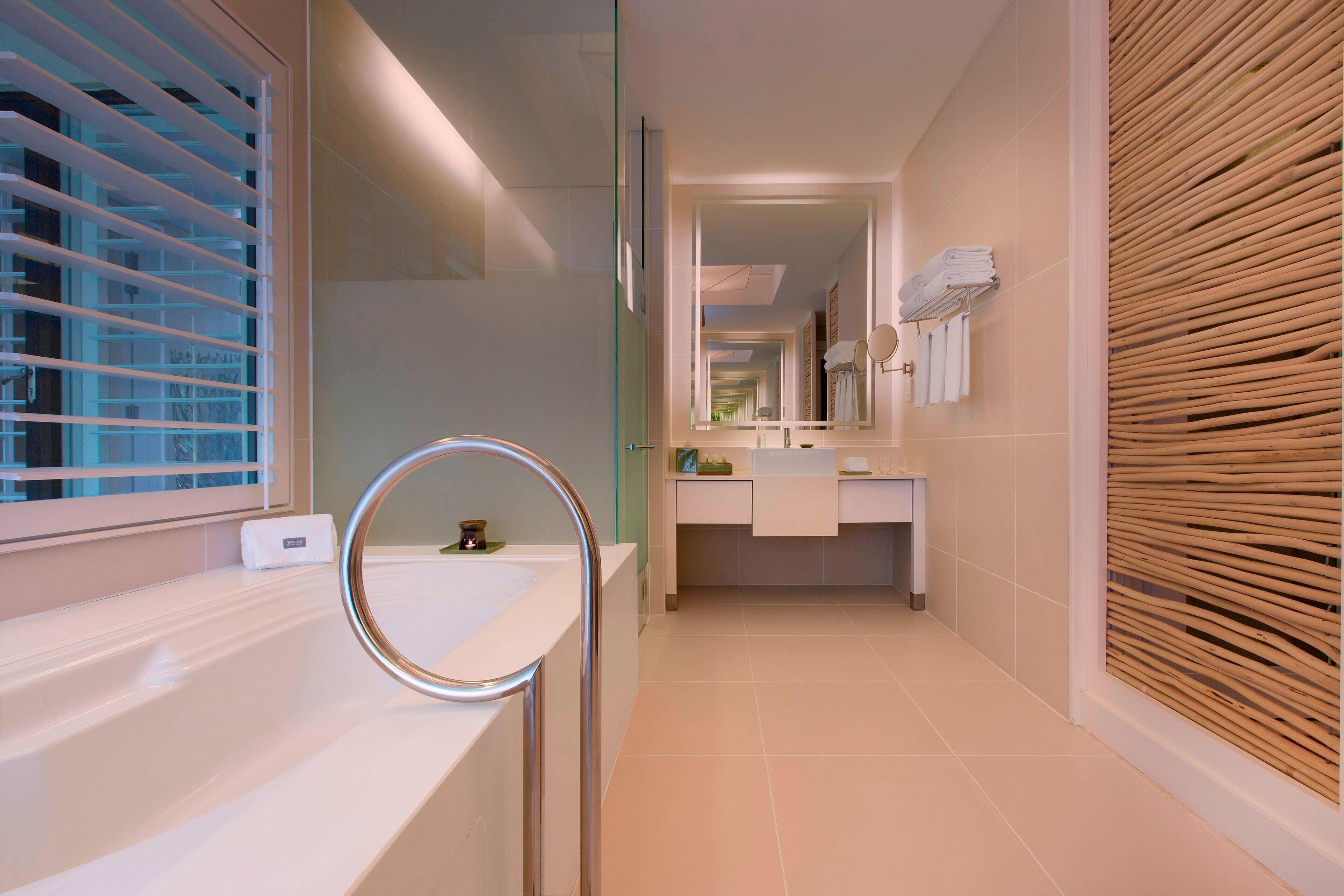Un baño moderno con mampara de vidrio, espejo redondo, lavabo blanco y panel de pared de madera.