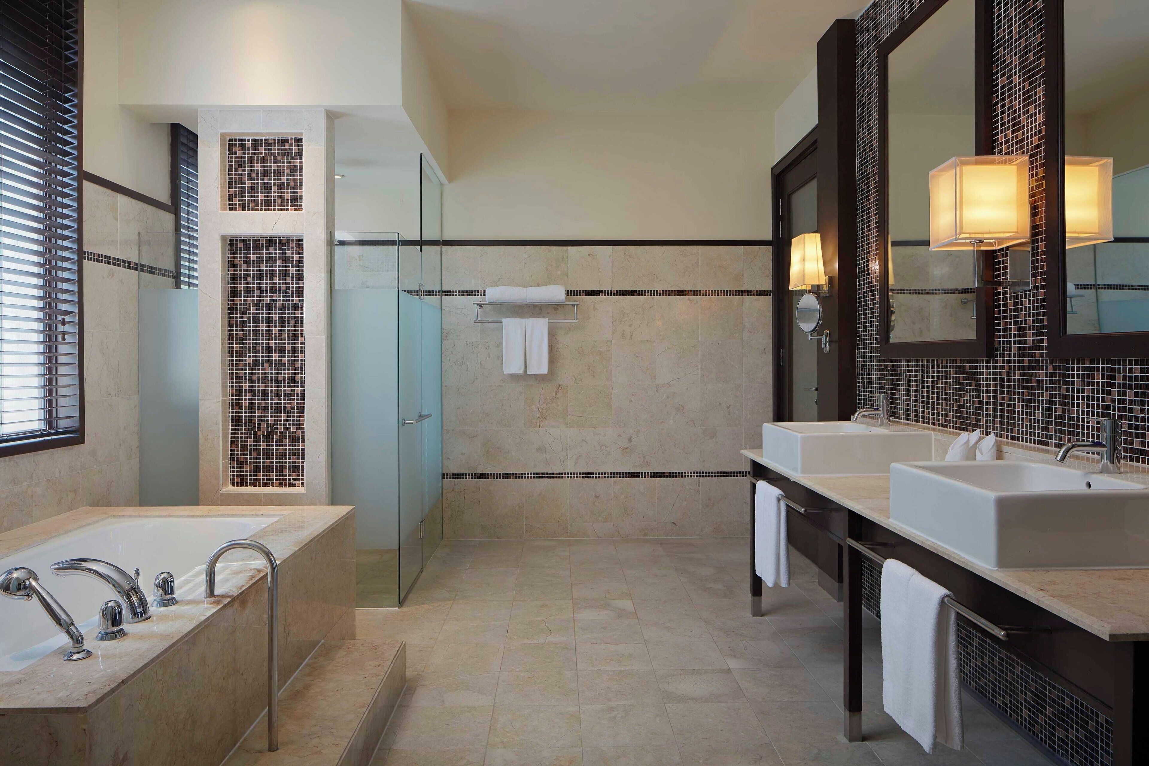 A modern bathroom with a large bathtub, two sinks, and a glass shower enclosure.