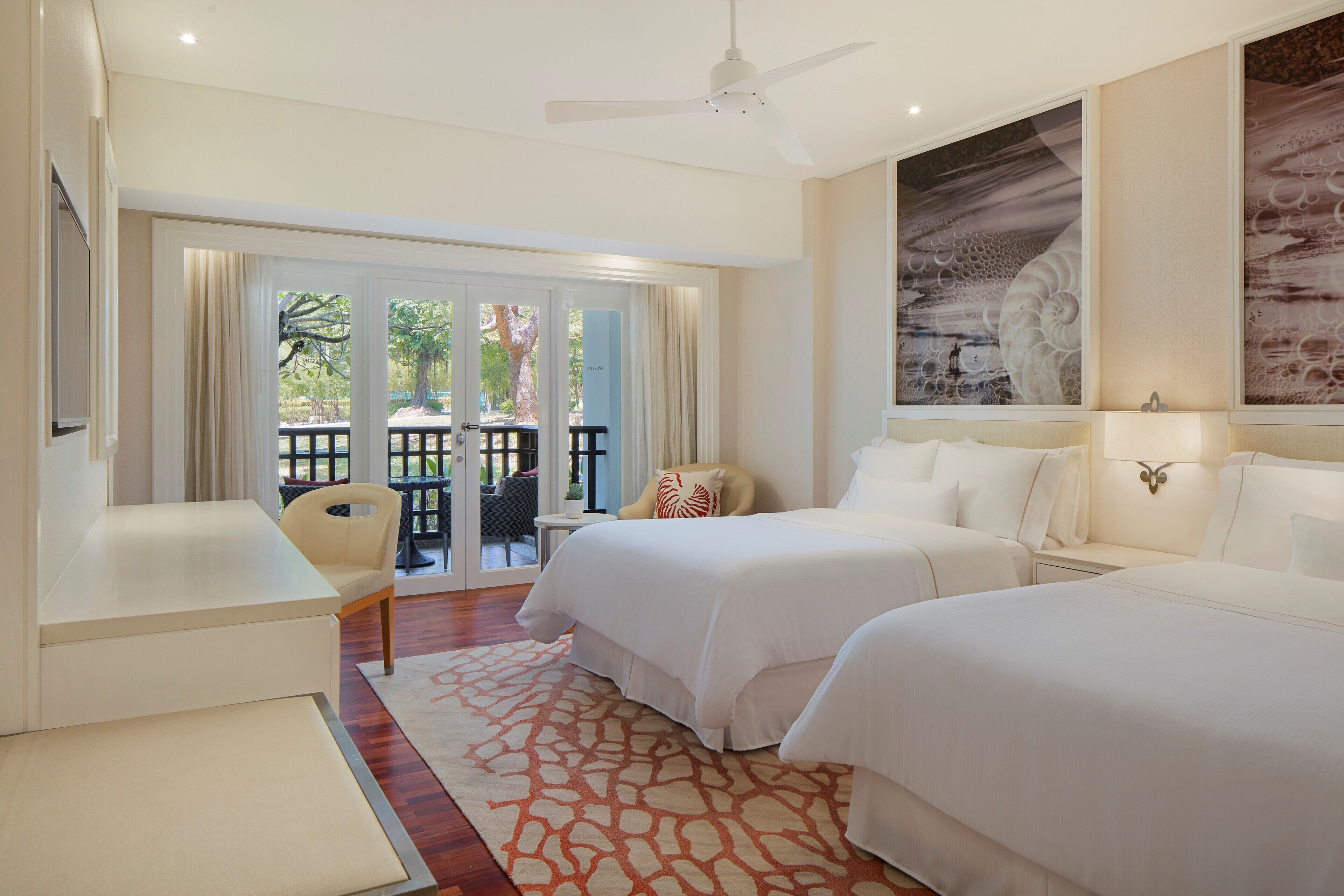 A hotel room with two beds, a desk, and a balcony with outdoor furniture.