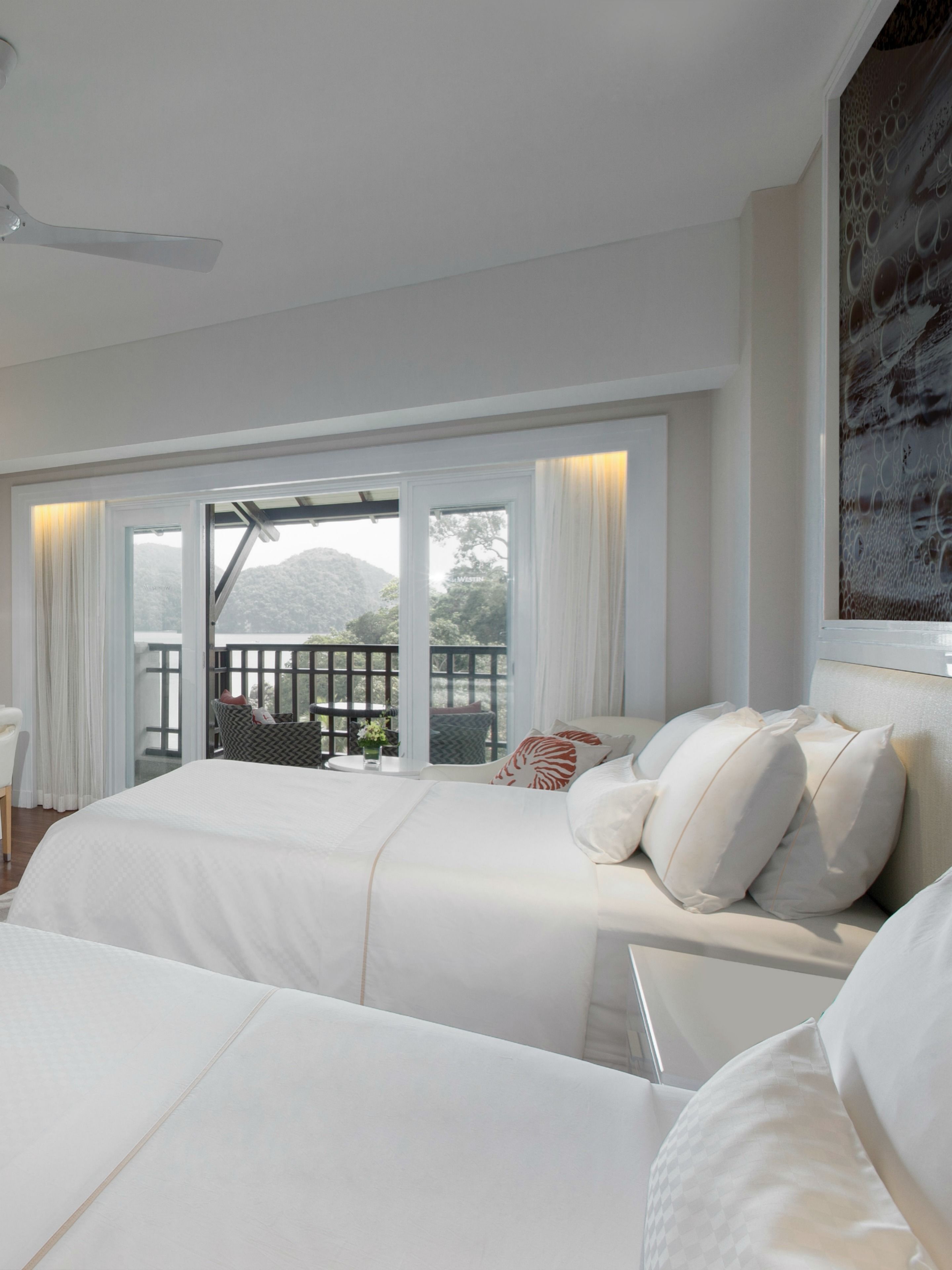 A hotel room with two beds, a balcony with a view of mountains, and a ceiling fan.