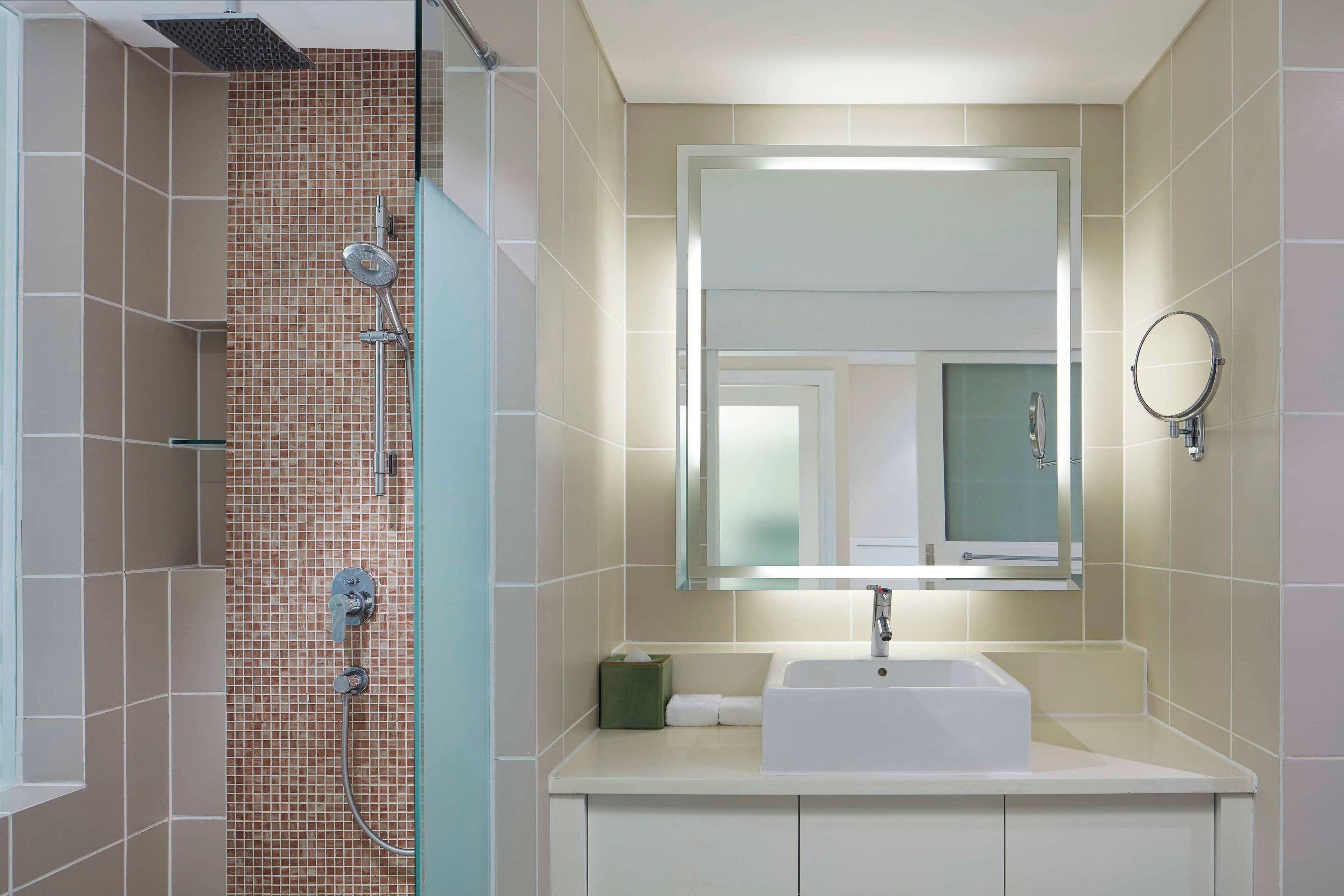 A bathroom with a shower, a sink, a mirror, and a towel dispenser.