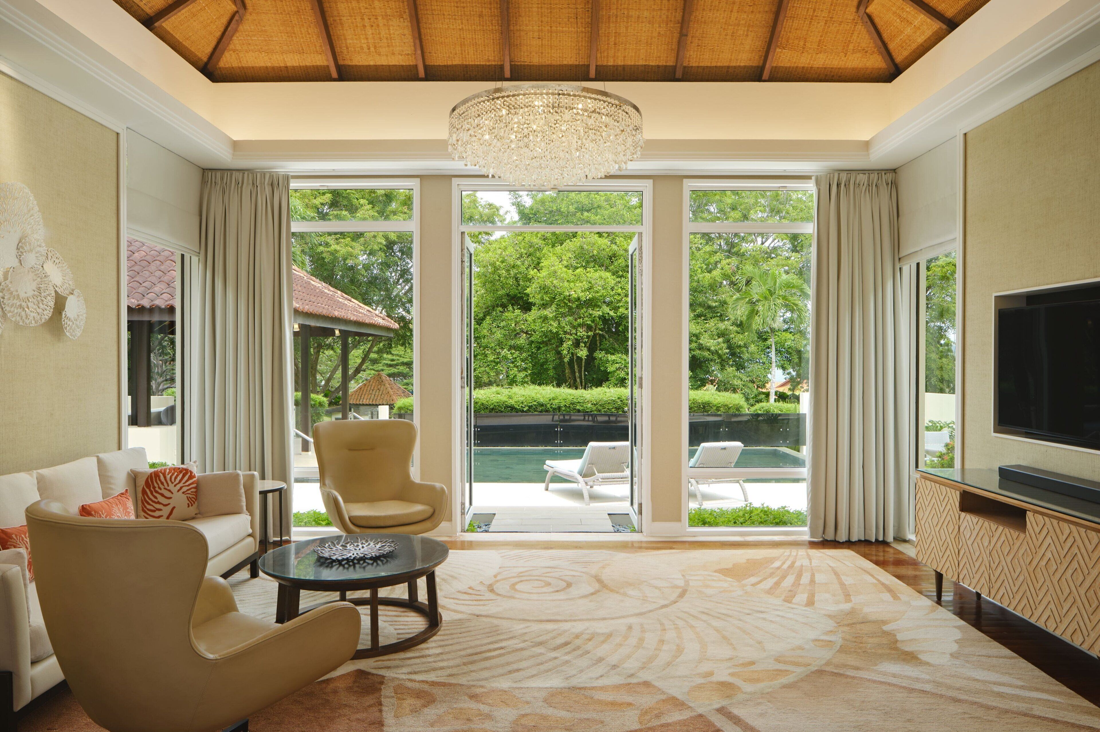 A spacious living room with a large window, a chandelier, and a flat-screen TV.