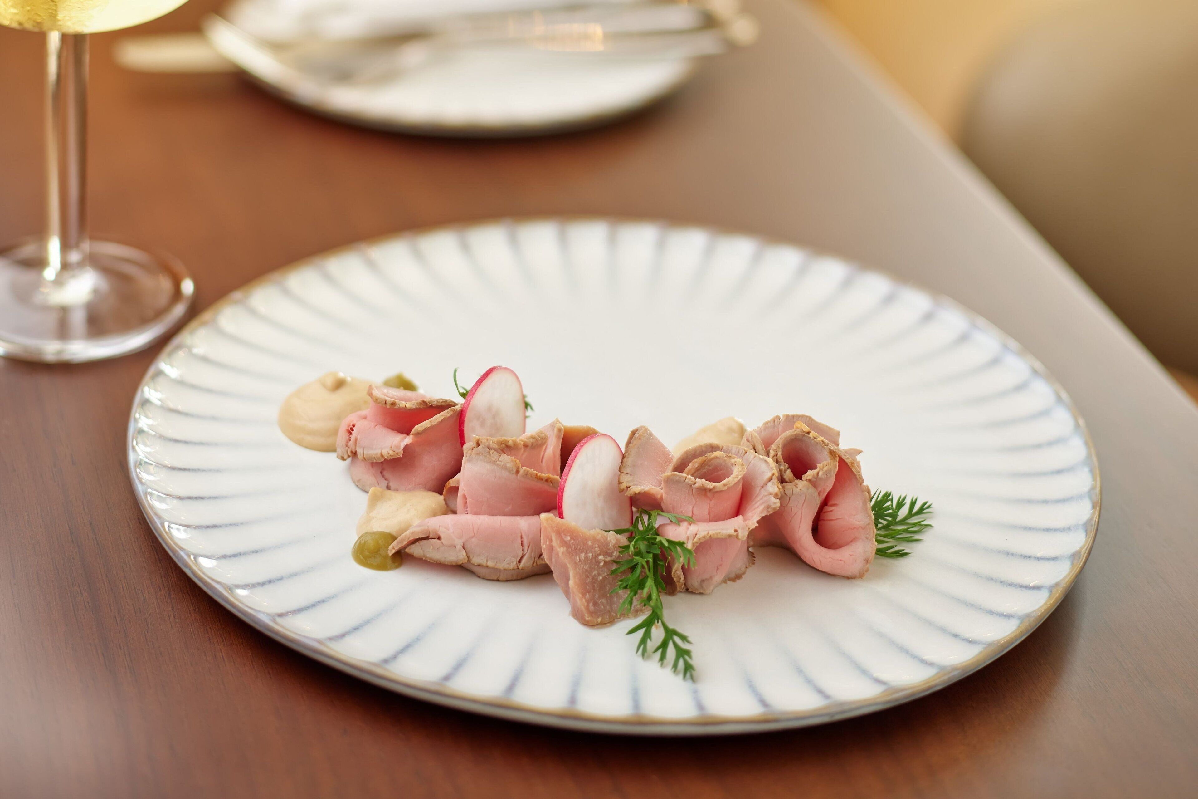 En tallrik med skivad kött, rädisa och örter, serverat på en vit tallrik.