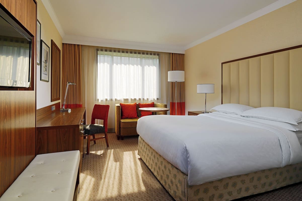 A hotel room with a large bed, a desk with a chair, a small table, and a sofa.