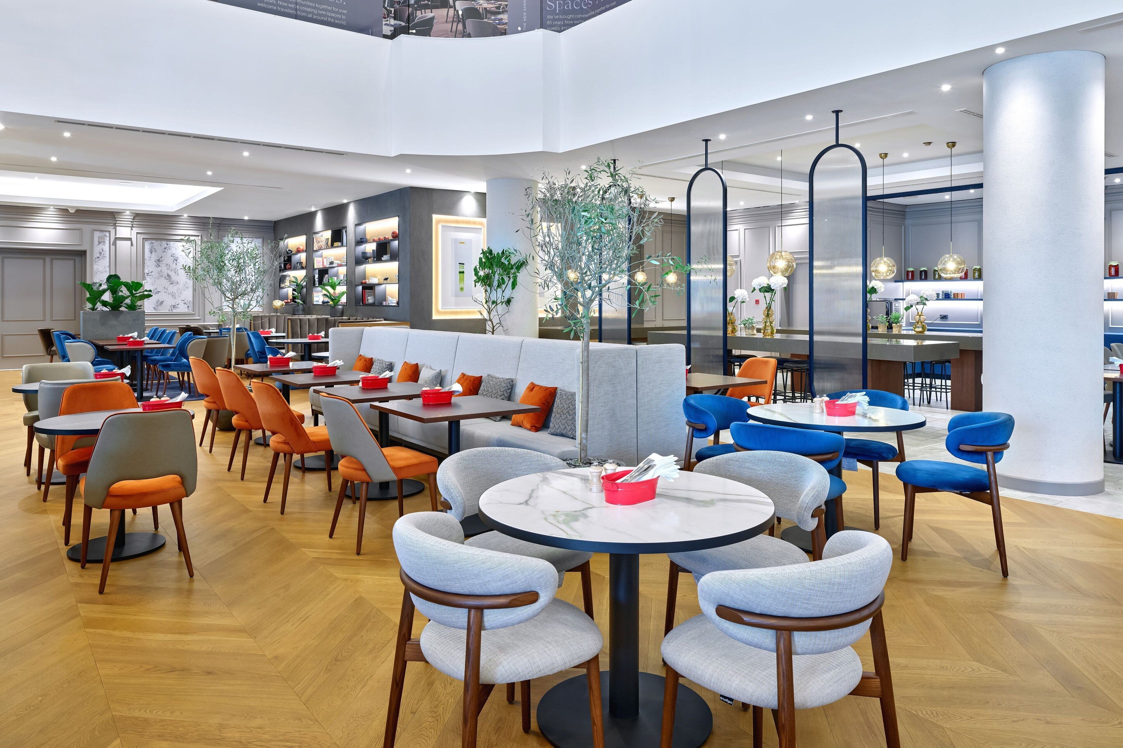 A modern restaurant with round tables and chairs, a bar area, and a seating section with a sofa and chairs.