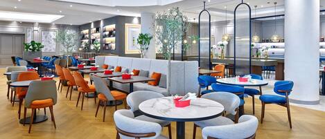 Un restaurante moderno con mesas y sillas redondas, una zona de bar y una sección con sofás y sillones.