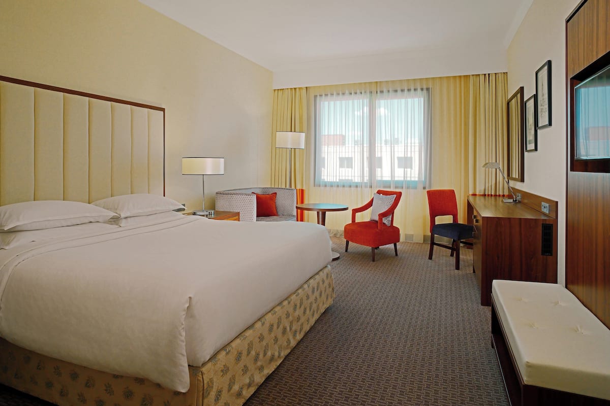 A hotel room with a large bed, a desk, a chair, a small table, and a television.