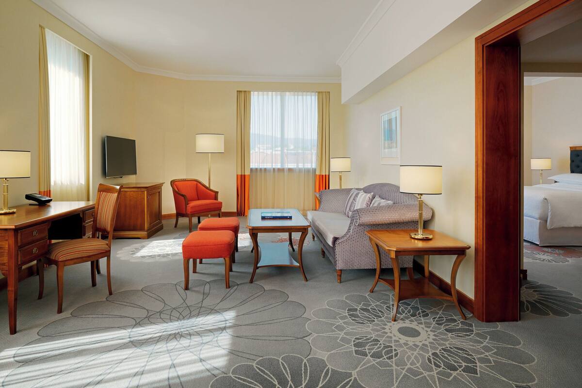 A hotel room with a bed, a desk, a chair, a sofa, and a TV.