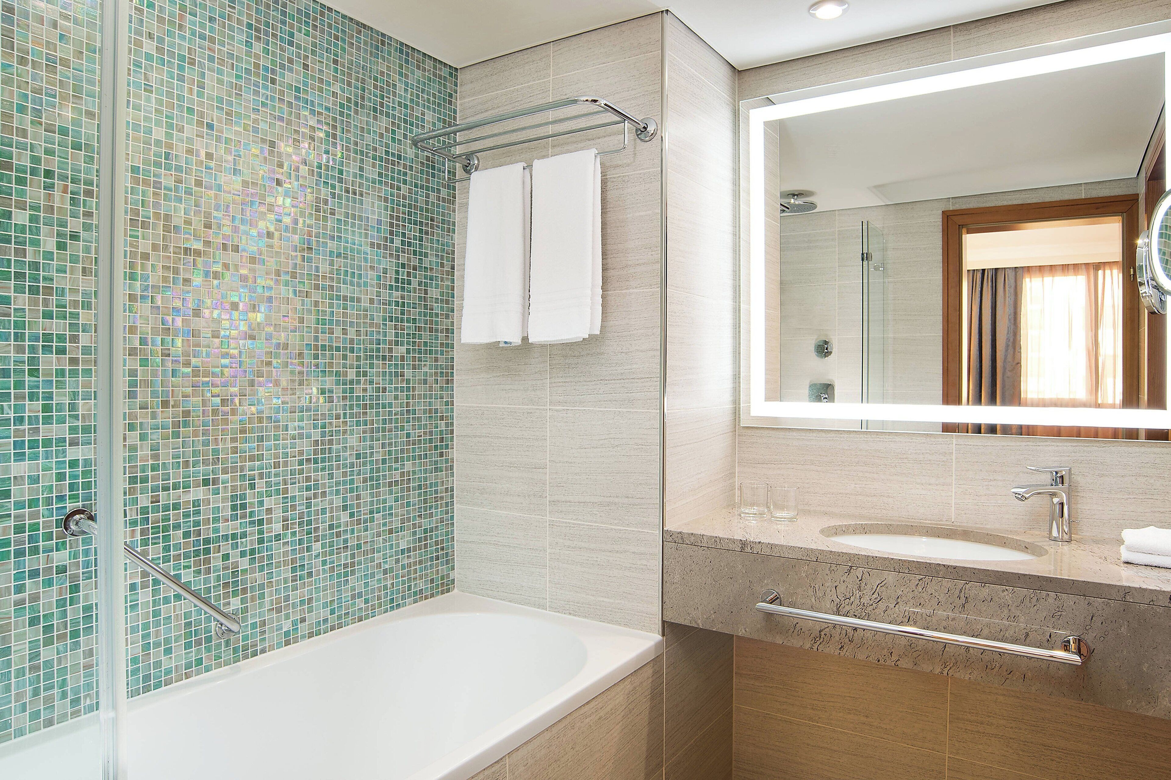 Un baño moderno con pared de mosaicos, cabina de ducha de vidrio, bañera y tocador con espejo.