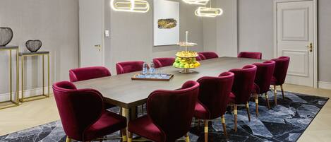 A conference room with a long table, red chairs, and a modern chandelier.