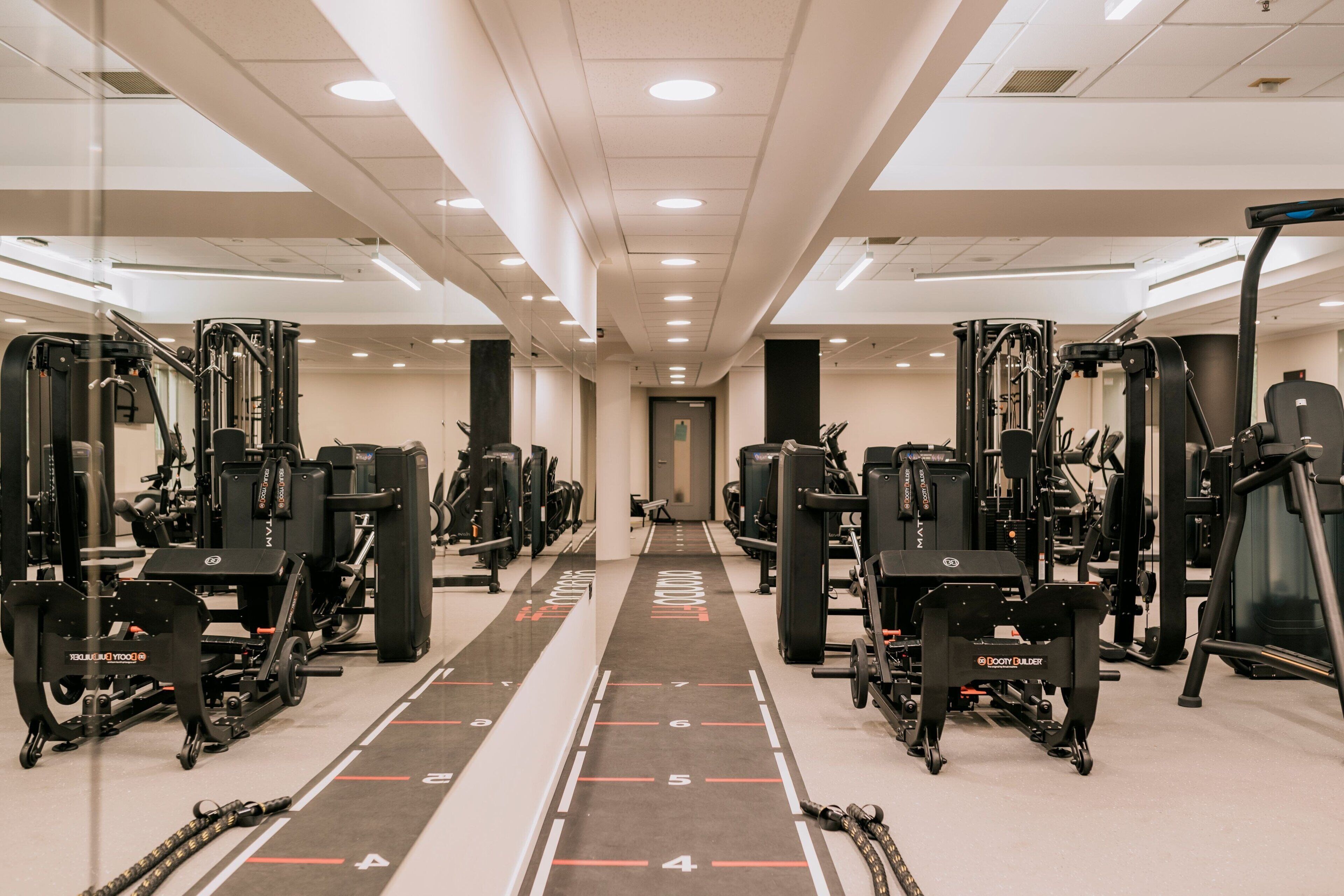 Une salle de sport équipée de divers appareils d’exercice et dotée d’un couloir central où sont indiqués des numéros.