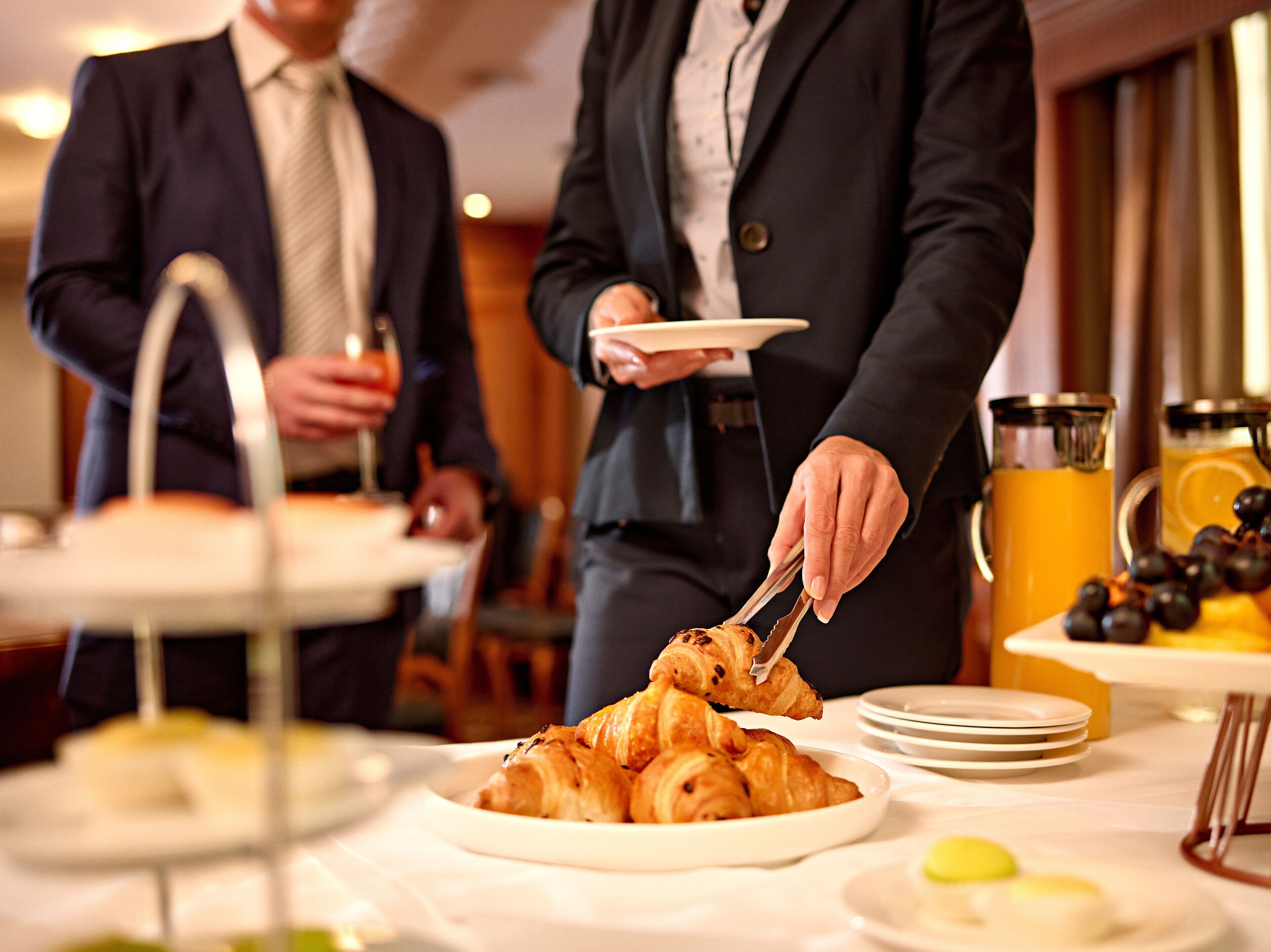 A breakfast buffet with croissants, a fruit platter, and a juice dispenser.