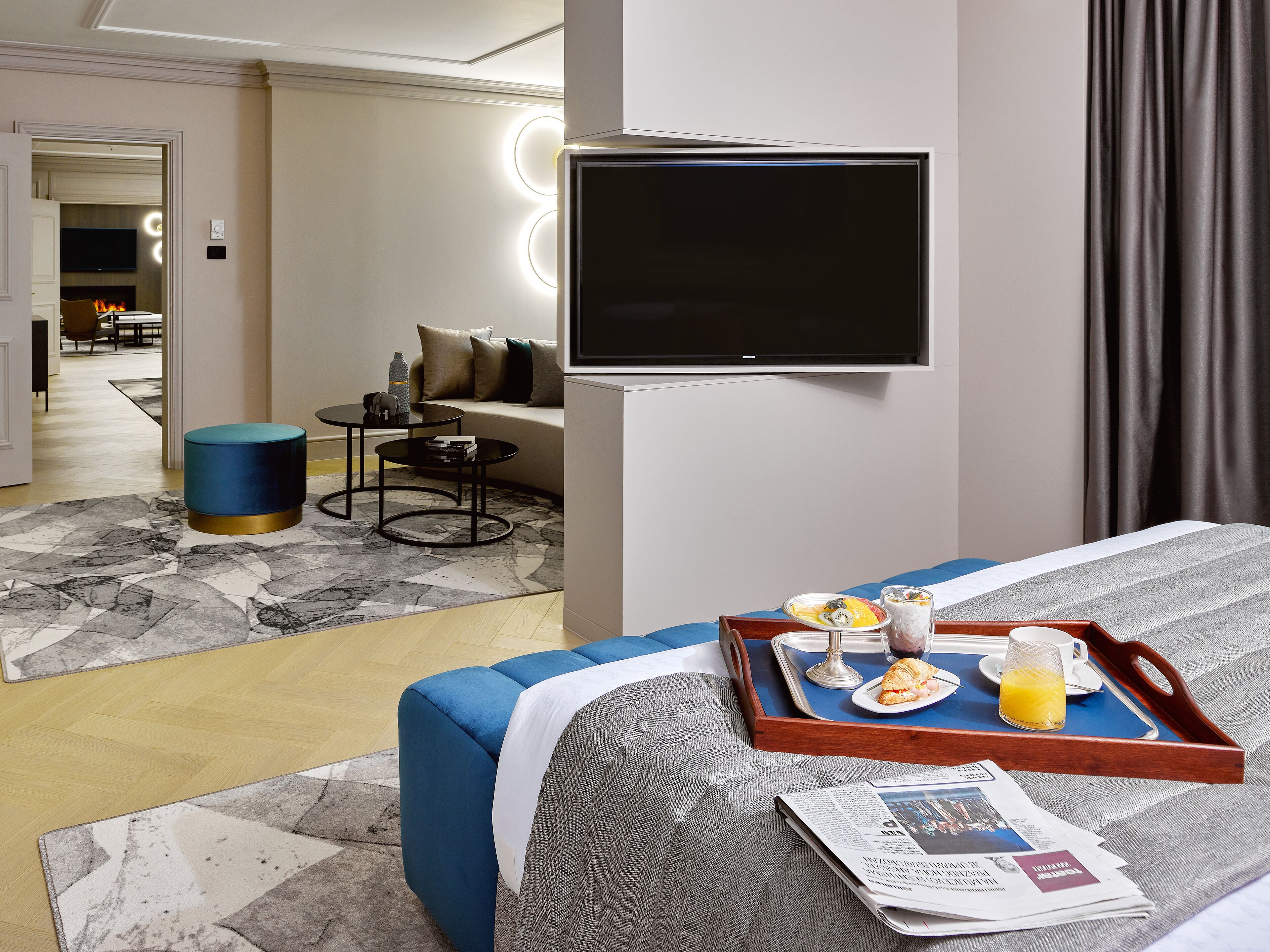 Een hotelkamer met een bed, een aan de muur bevestigde televisie, een eettafel met ontbijtartikelen en een bankstel op de achtergrond.