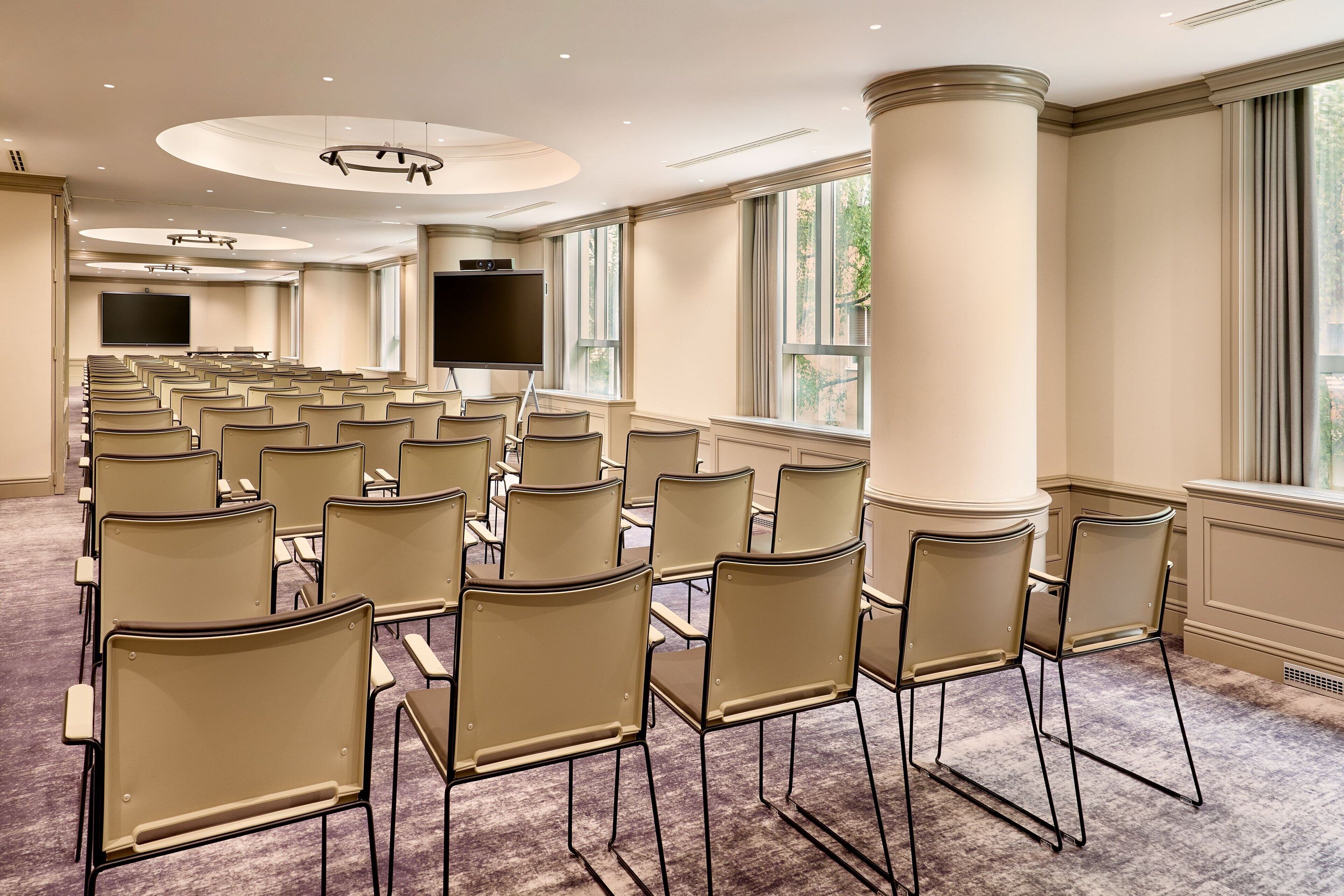 Un salón de conferencias con filas de sillas, una pantalla grande y ventanas con cortinas.