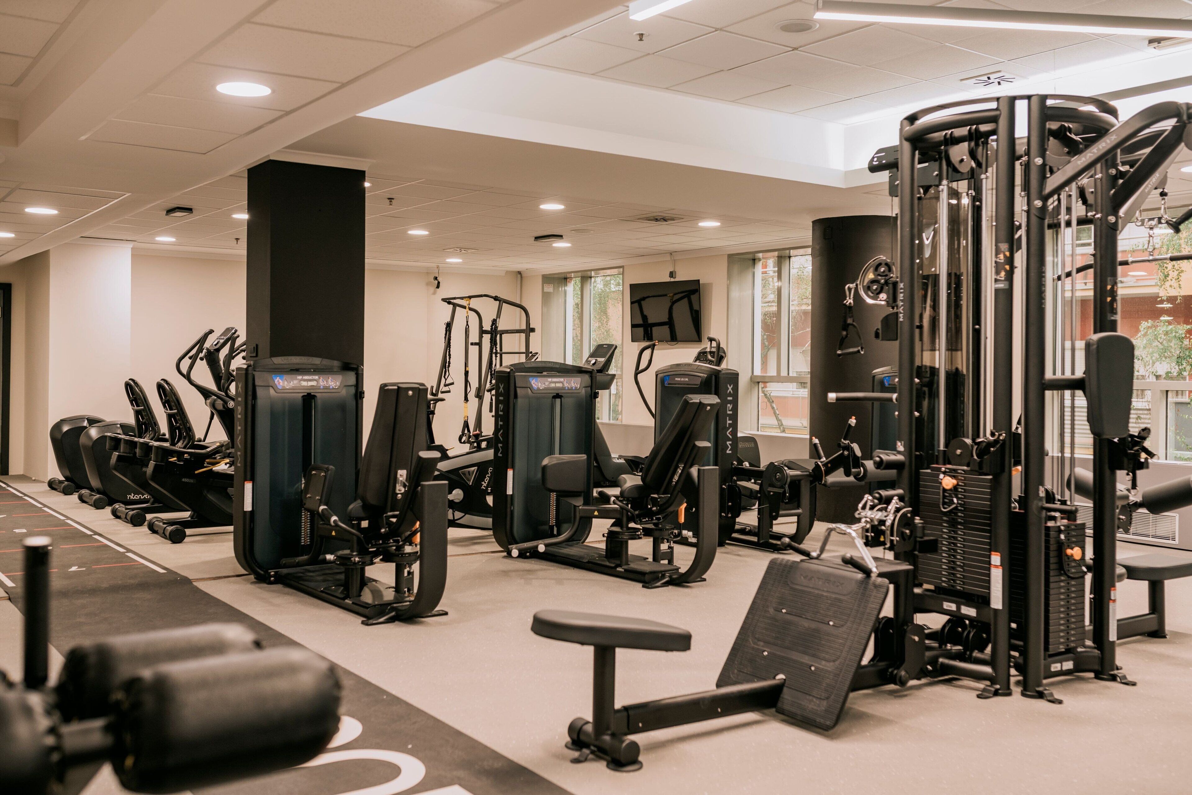Een sportschool met diverse fitnessapparaten, een bank en een aan de muur bevestigde televisie.