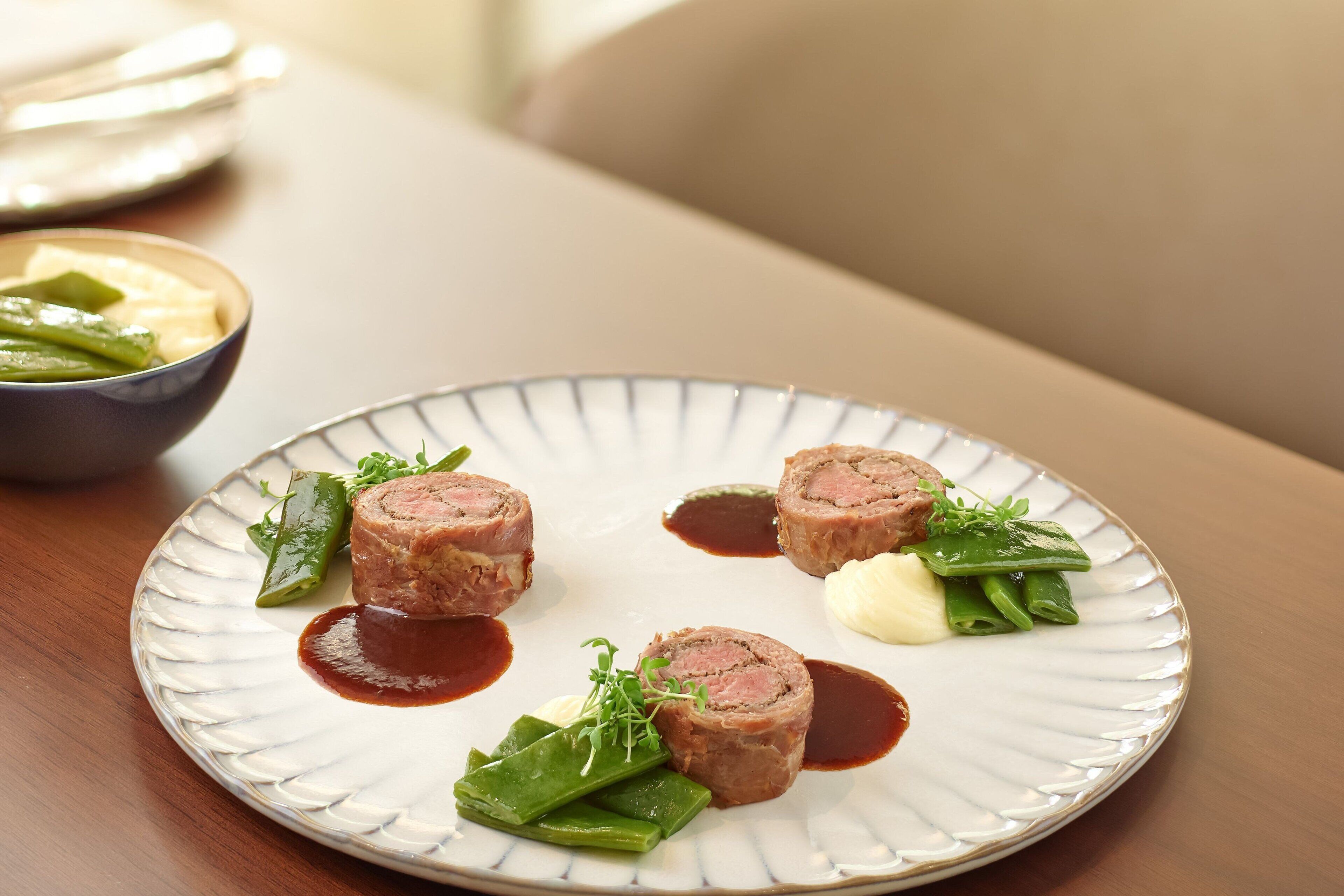 Un plato de comida con rollos de carne y verduras sobre un plato blanco.