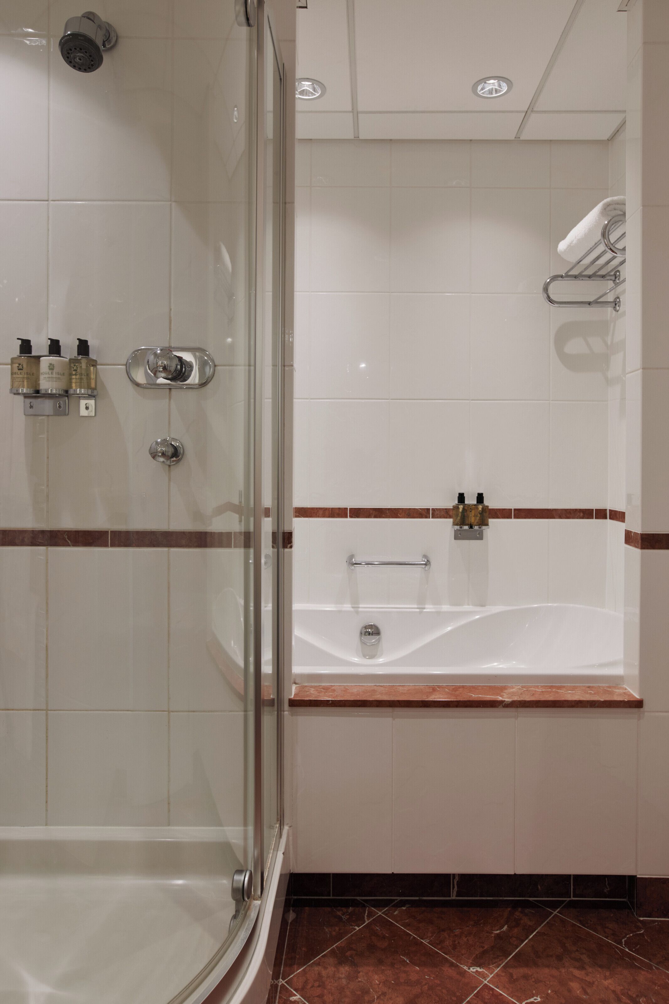 A bathroom with a glass-enclosed shower, a bathtub, and a towel rack.