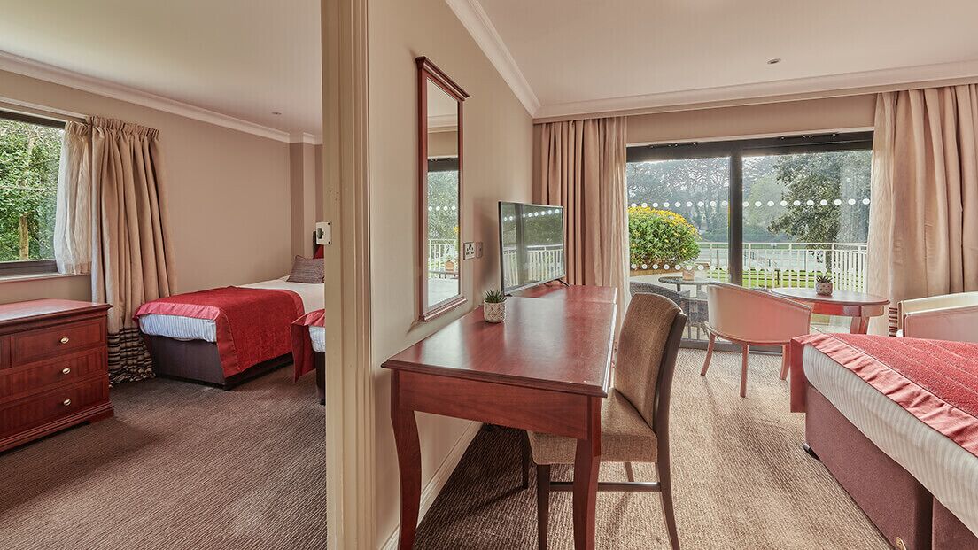 Una habitación de hotel con cama, escritorio, silla, cómoda y un gran ventanal con cortinas.