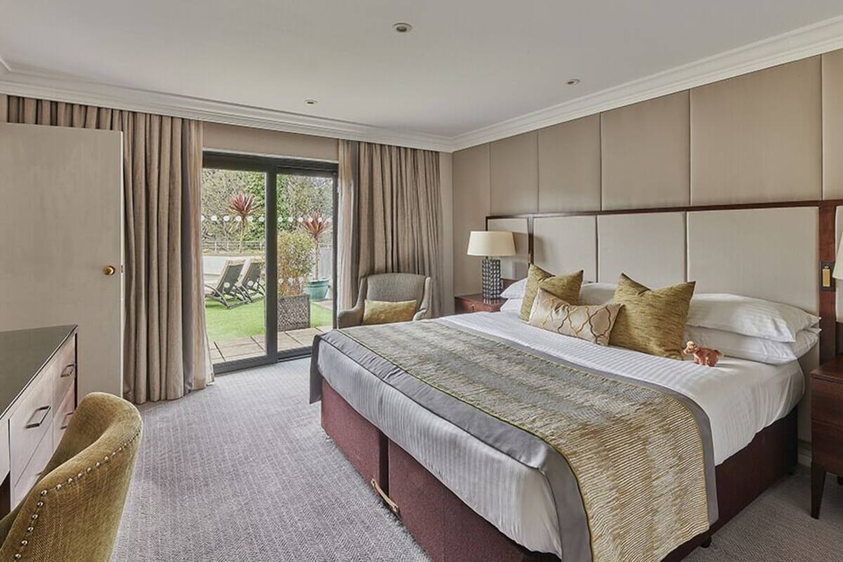 A hotel room with a large bed, a desk, a chair, and a view of the outdoors.