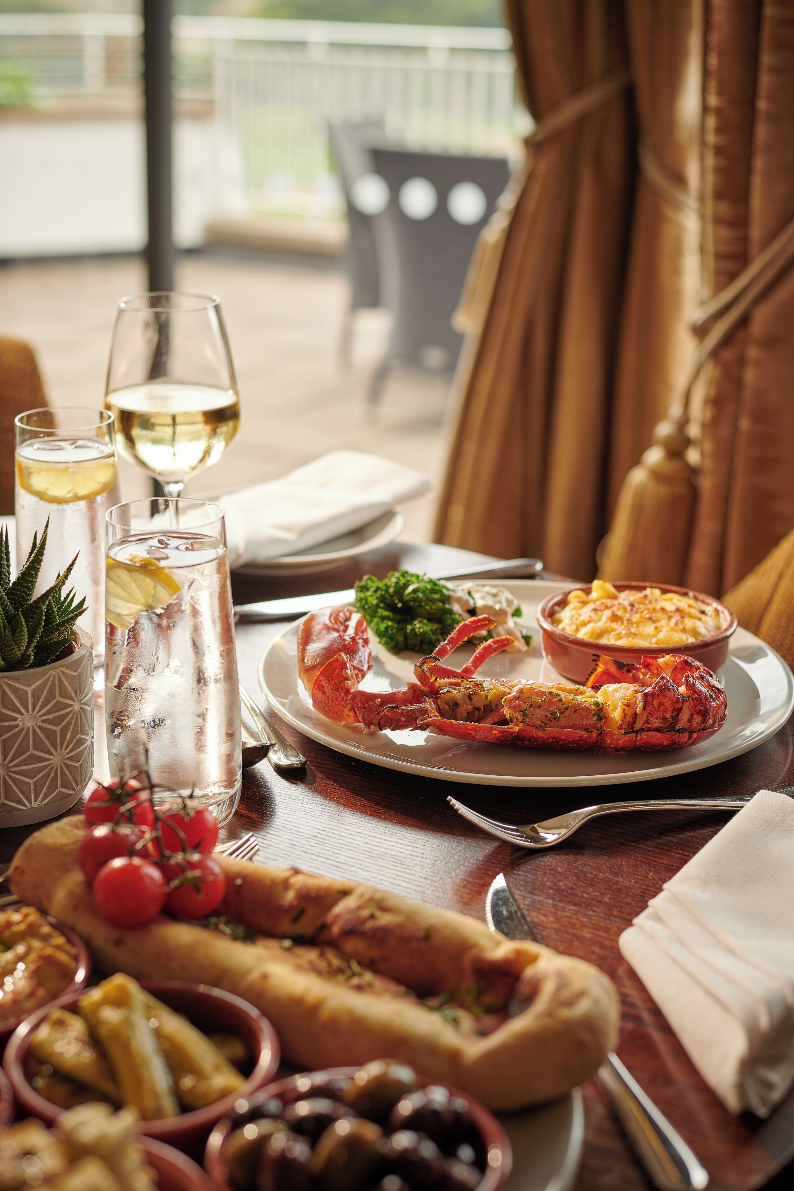 A dining table with a lobster, a bowl of pasta, and various side dishes.