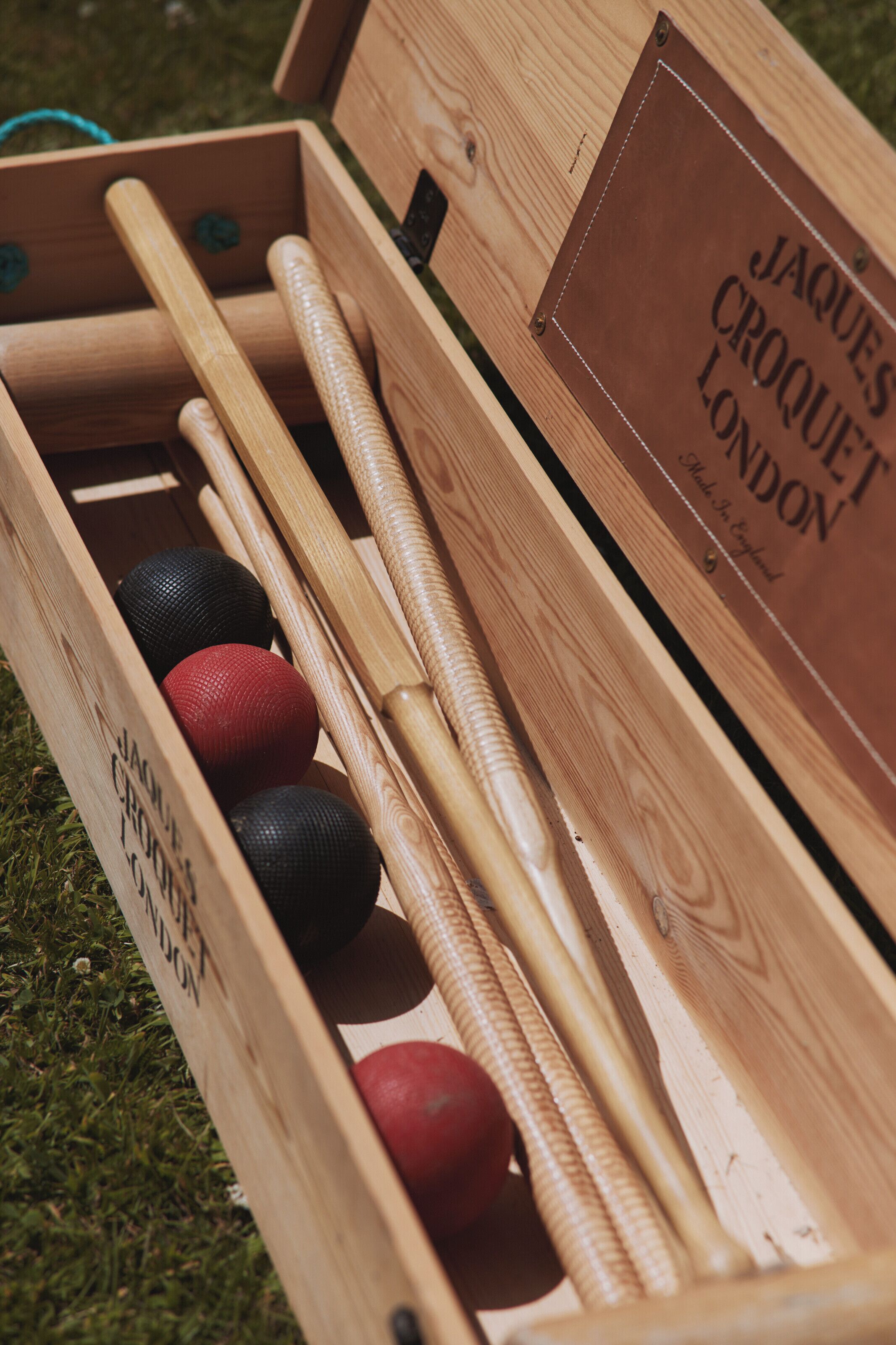 Une boîte en bois contenant des maillets et des balles de croquet, portant l’inscription « JAQUES CROQUET LONDON ».