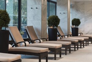 Una hilera de sillones con cojines, ubicados en un espacio interior iluminado por grandes ventanales y plantas en macetas.