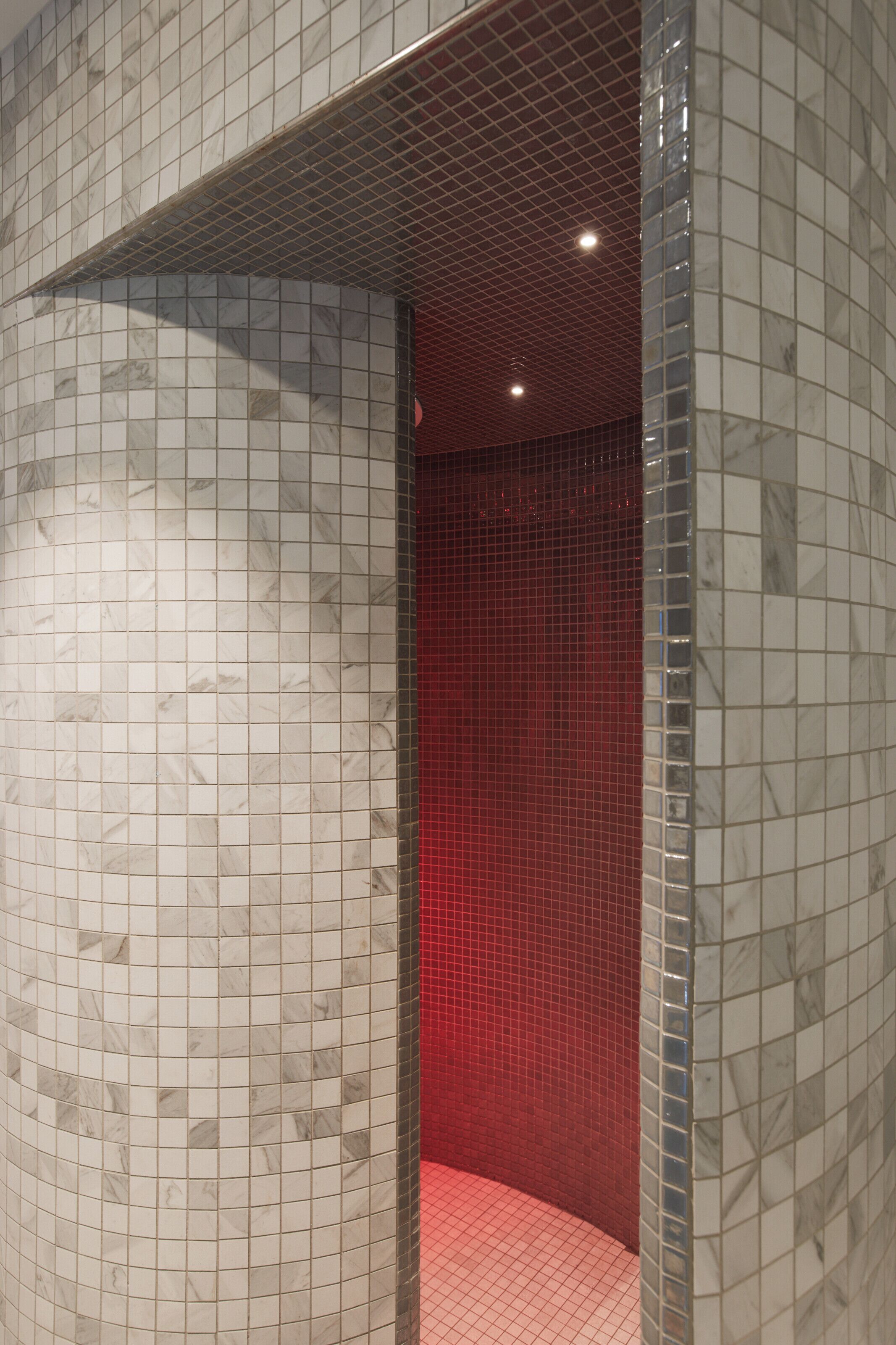 A tiled bathroom with a curved wall and a red-tiled accent wall.