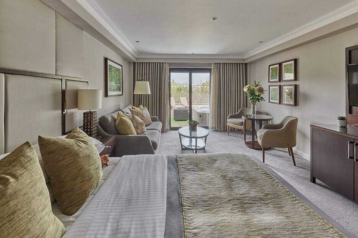 A hotel room with a bed, sofa, armchair, small table, TV, and a view of the outdoors.
