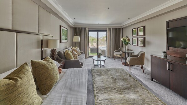 A hotel room with a bed, sofa, armchair, small table, TV, and a view of the outdoors. - St Pierre Park Hotel & Golf (St. Peter Port)