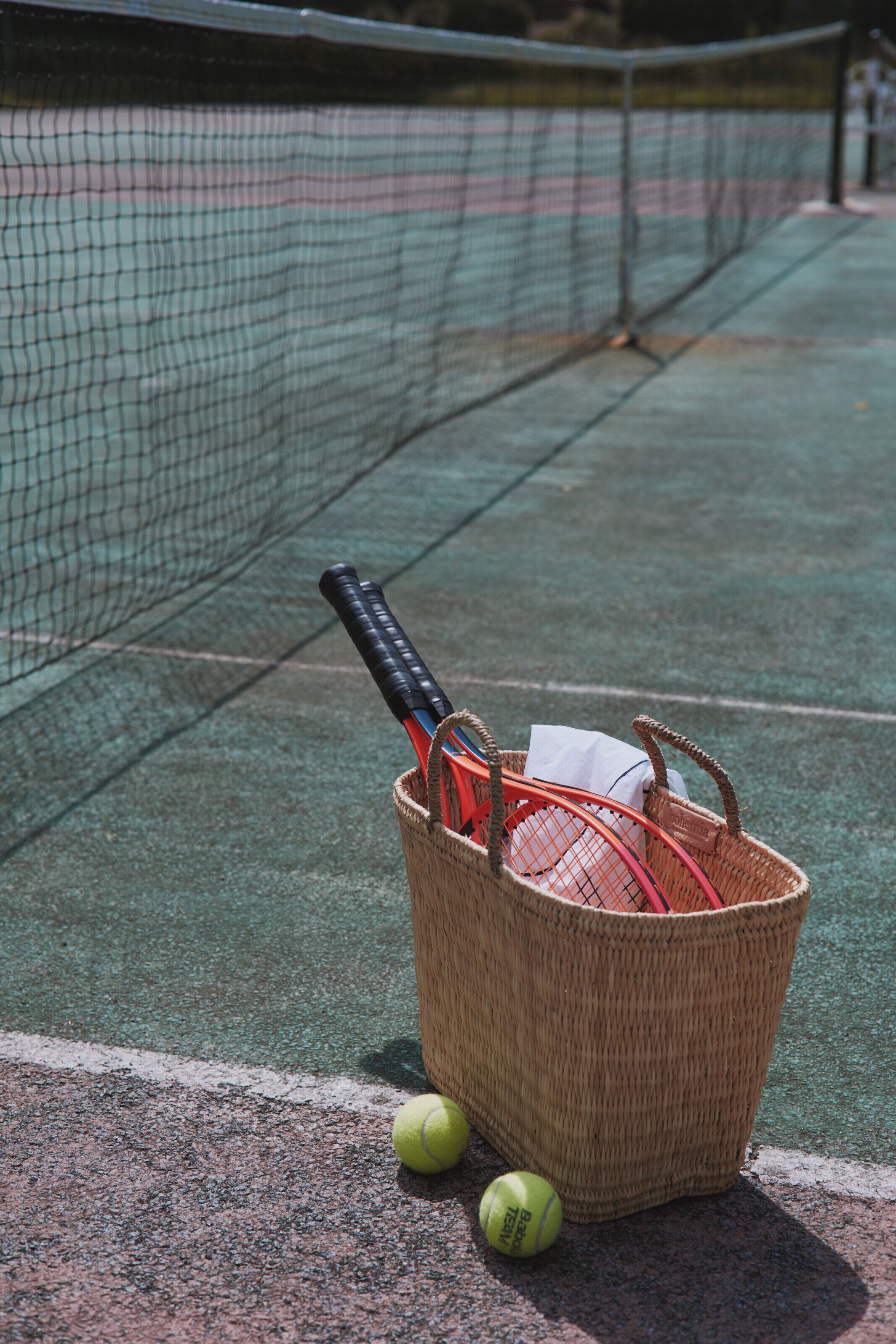 Una cancha de tenis con una cesta que contiene una raqueta, una pelota y un ovillo de lana.