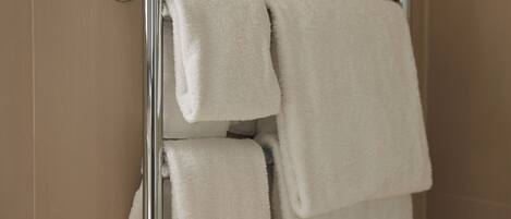 Un baño con mampara de vidrio, un perchero con toallas dobladas y paredes de azulejos color beige.