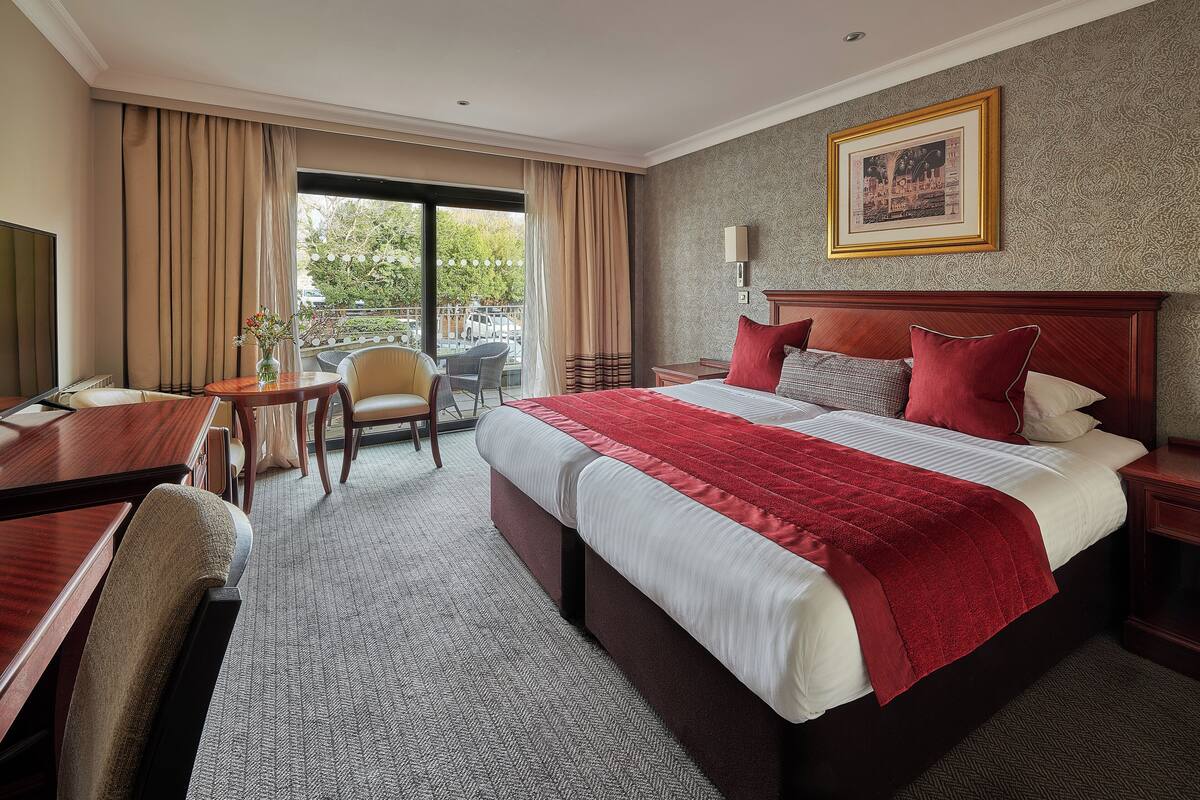 A hotel room with a large bed, a desk, a chair, and a view of the outdoors.
