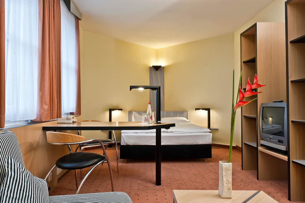 Een hotelkamer met een bed, een bureau met stoel, een televisie en een plant.