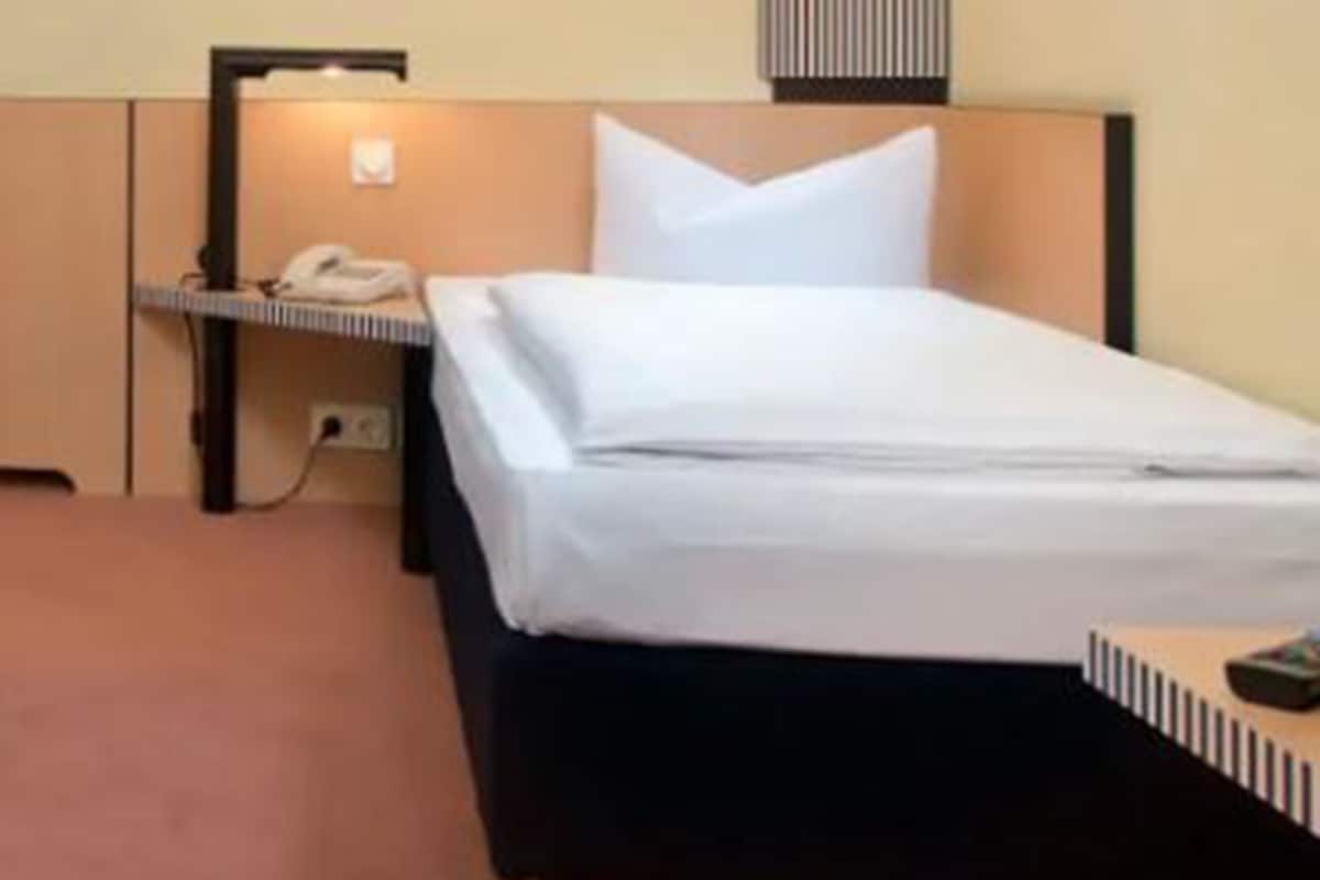 Een hotelkamer met een bed, nachtkastje, lamp en een wandlamp.
