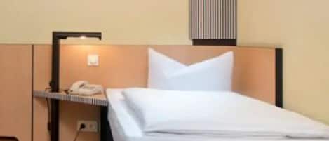 A hotel room with a bed, a bedside table, a lamp, and a wall-mounted light fixture.