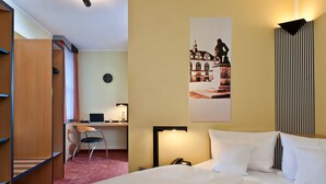 Une chambre d’hôtel équipée d’un lit, d’un bureau, d’une chaise et d’une lampe fixée au mur.