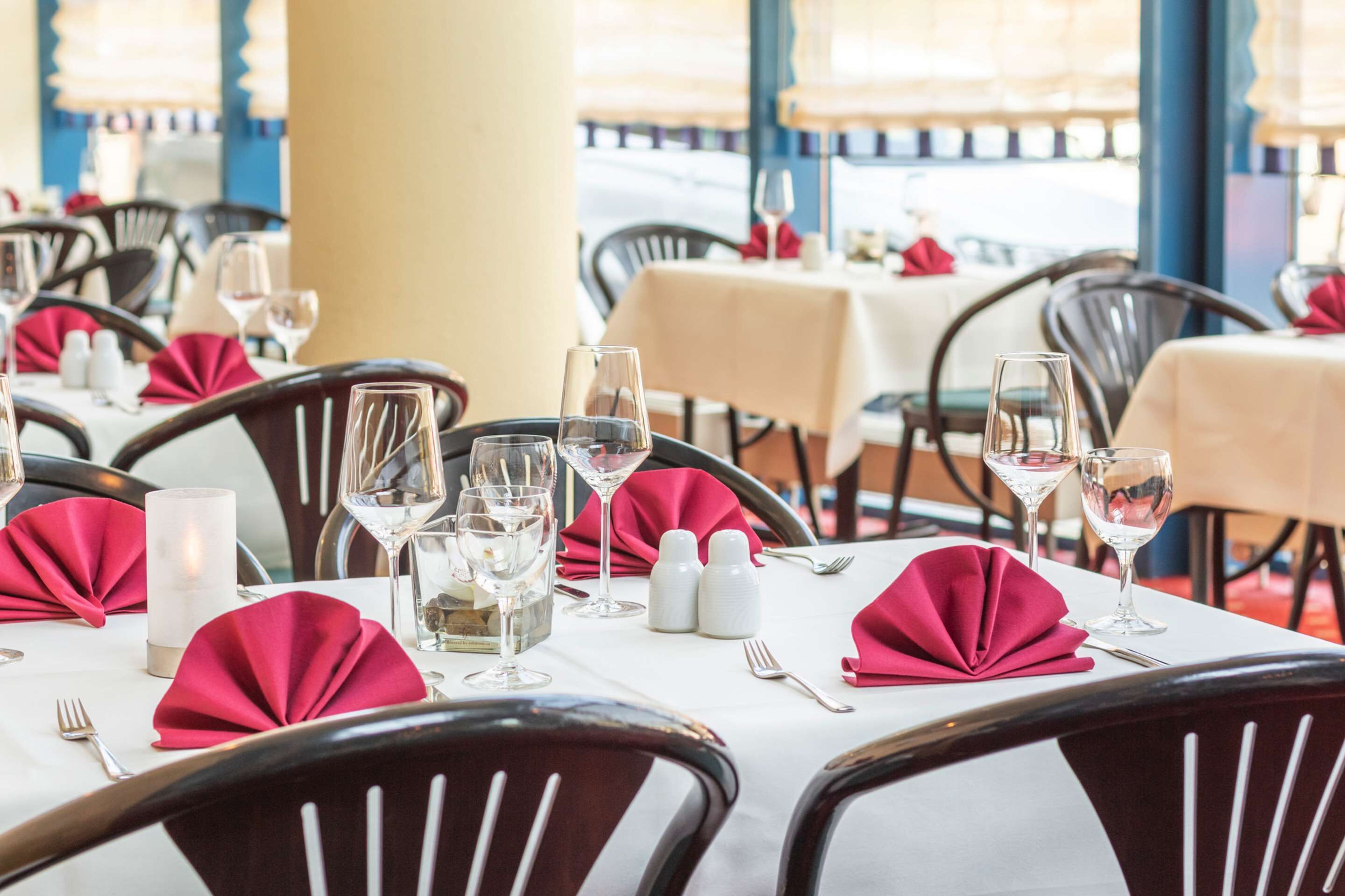 A restaurant with tables set for dining, featuring red napkins and clear glassware.
