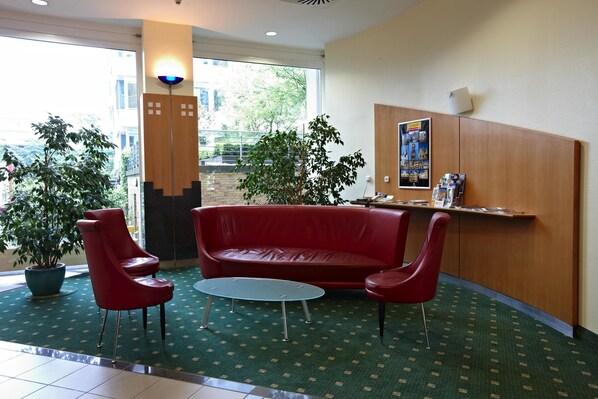 A lobby with a red sofa, two red chairs, a small round table, and a potted plant.