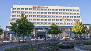 A multi-story InterCity Hotel with a modern facade, a parking area with several cars, and a landscaped garden with flowers and trees in front.