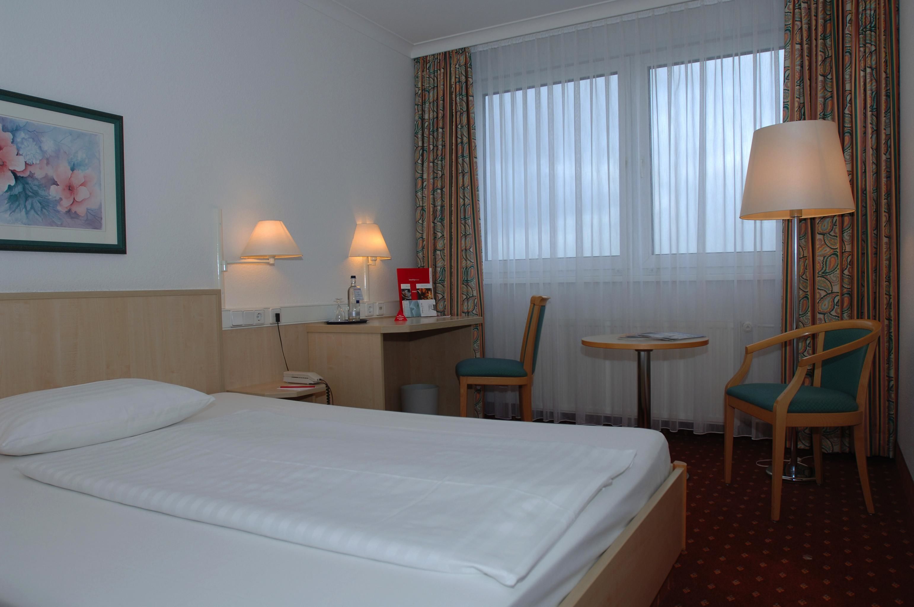 A hotel room with a bed, two chairs, a desk with a lamp, and a small table.