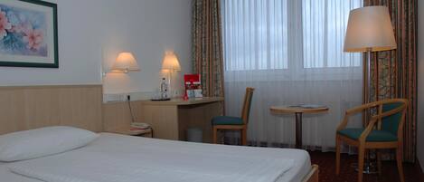 Et hotelværelse med en seng, to stole, et skrivebord med lampe og et lille bord.