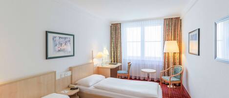 A hotel room with two beds, a desk, a chair, a small table, and a window with curtains.