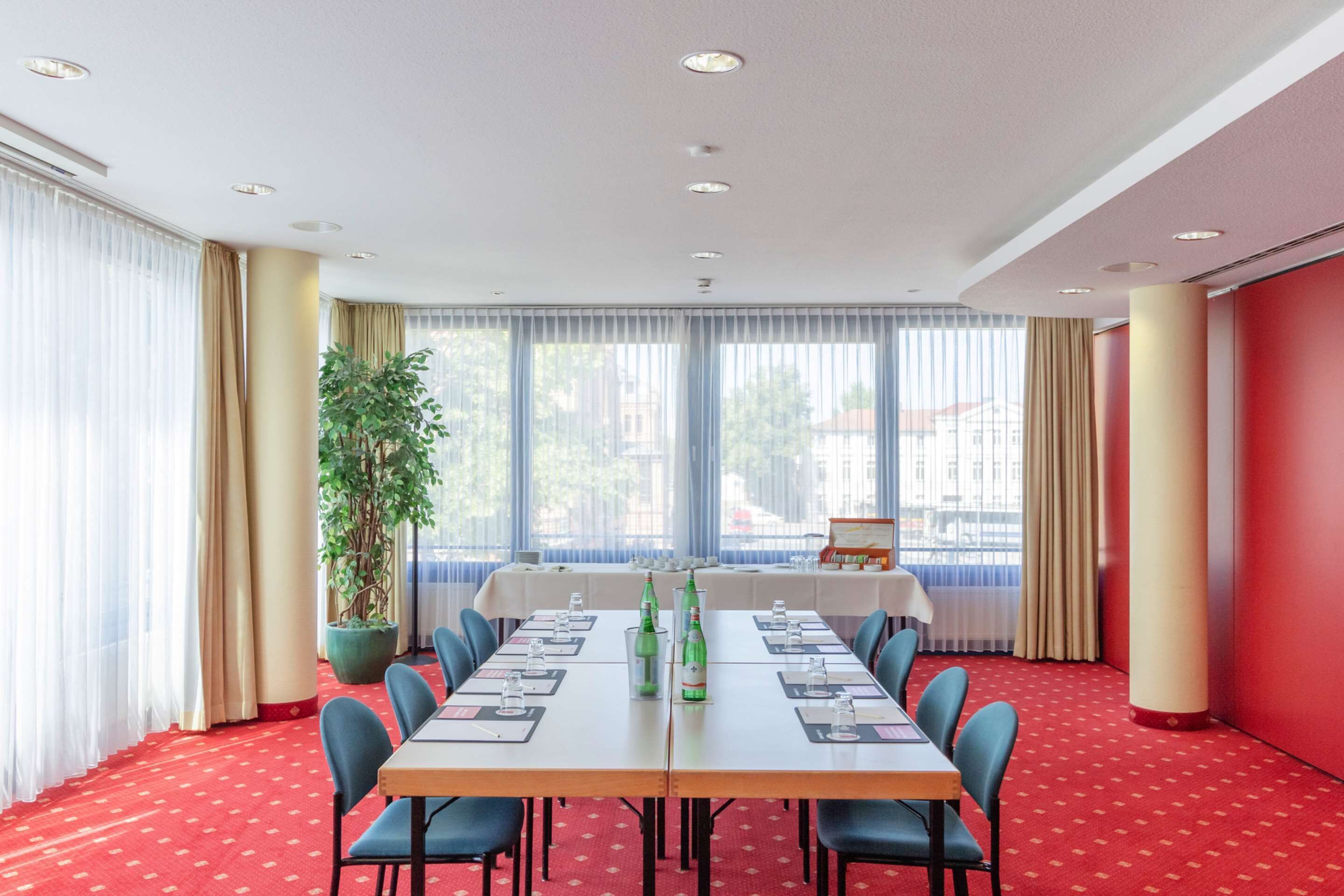 Une salle de conférence avec une longue table, des chaises bleues et une plante en pot.