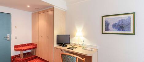 A hotel room with a desk, chair, television, and a framed picture on the wall.